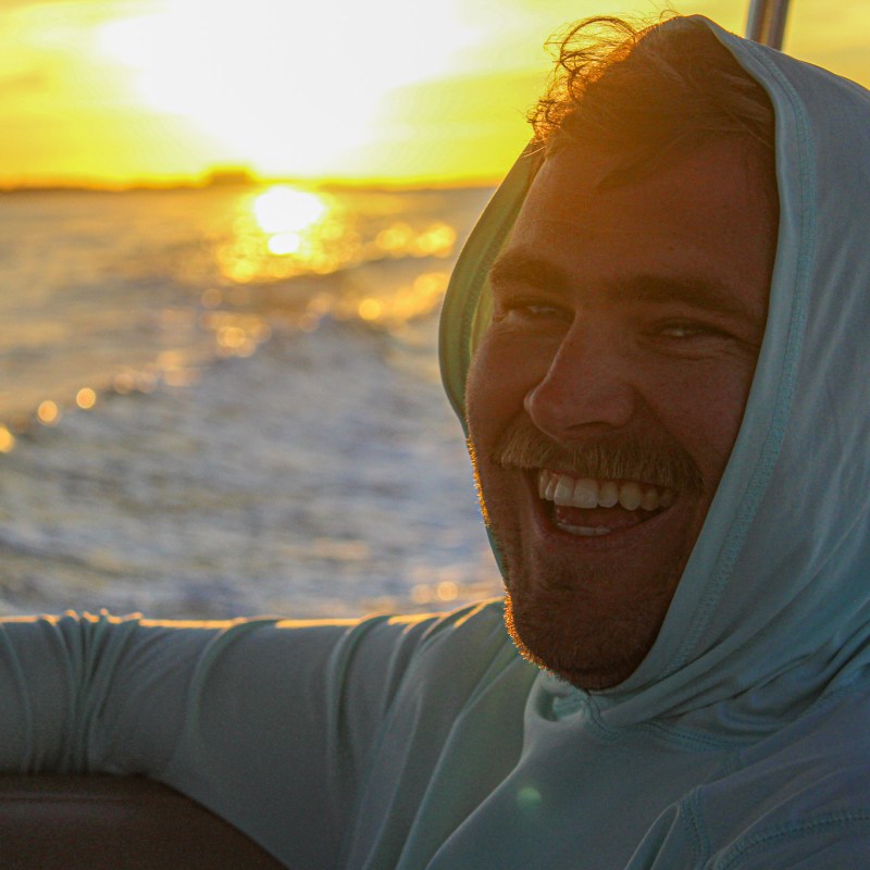 a man with long hair and a sunset in the background
