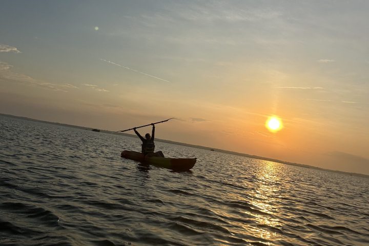 Person kayaking on calm water at sunset.