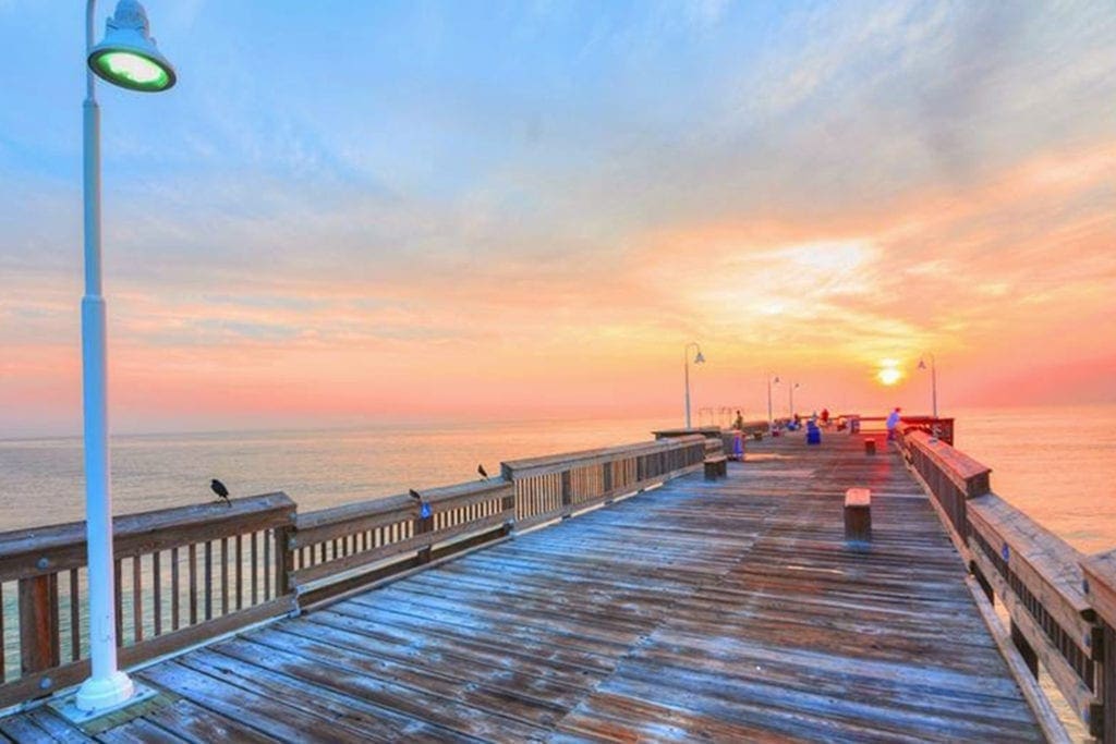Wooden pier over the ocean at sunset with a colorful sky and lamp posts.
